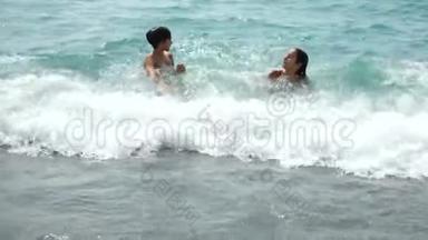 一家人，带着两个孩子，一对兄妹在岸边的海浪中飞溅。 他们抓住海浪